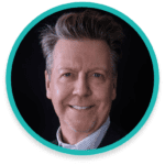 A man with short, styled hair and a light beard is smiling at the camera. He is wearing a collared shirt and a blazer. The image is framed with a circular teal border. The background is black.