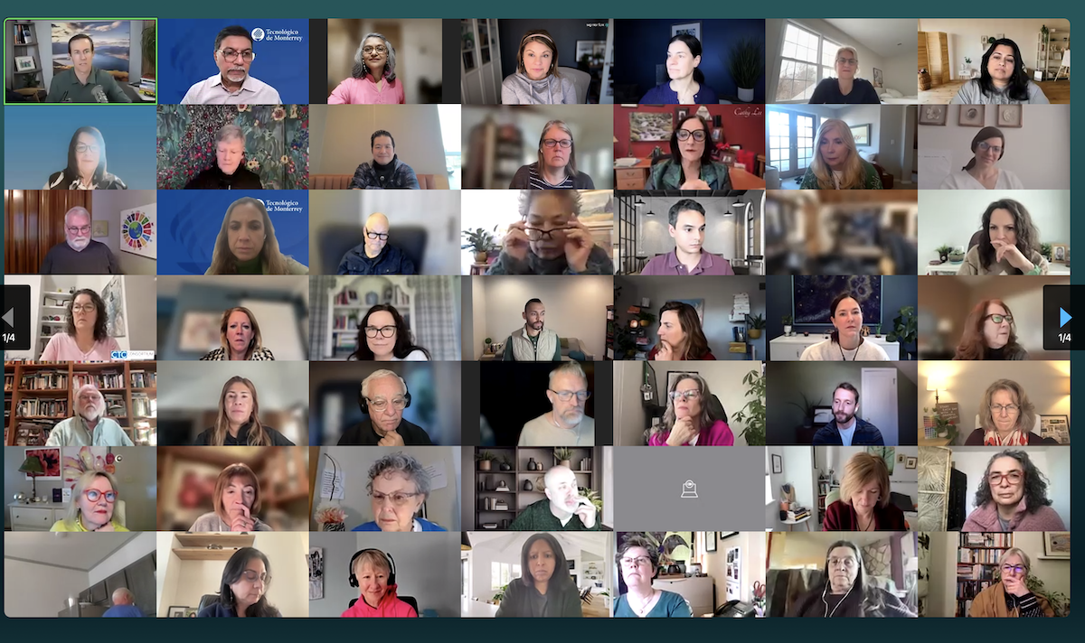 A virtual meeting with over 50 participants shown in a grid of video call windows, featuring a diverse group of people in different indoor settings, some looking at cameras, others speaking or listening, with one window displaying a muted icon.