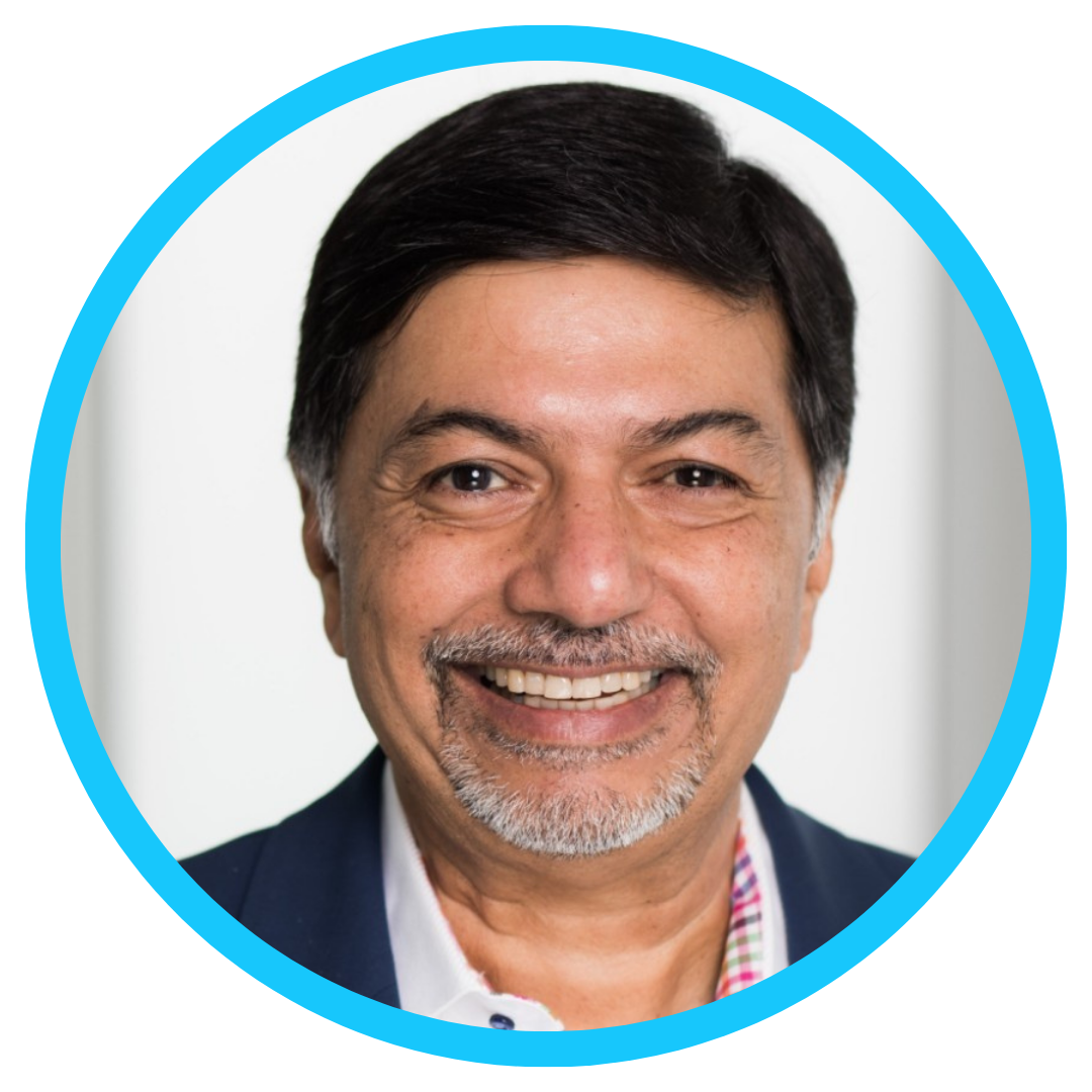 A middle-aged man with short dark hair, a trimmed beard, and mustache is smiling. He is wearing a navy blazer over a multicolored-collared shirt, and the image is framed by a bright blue circle.